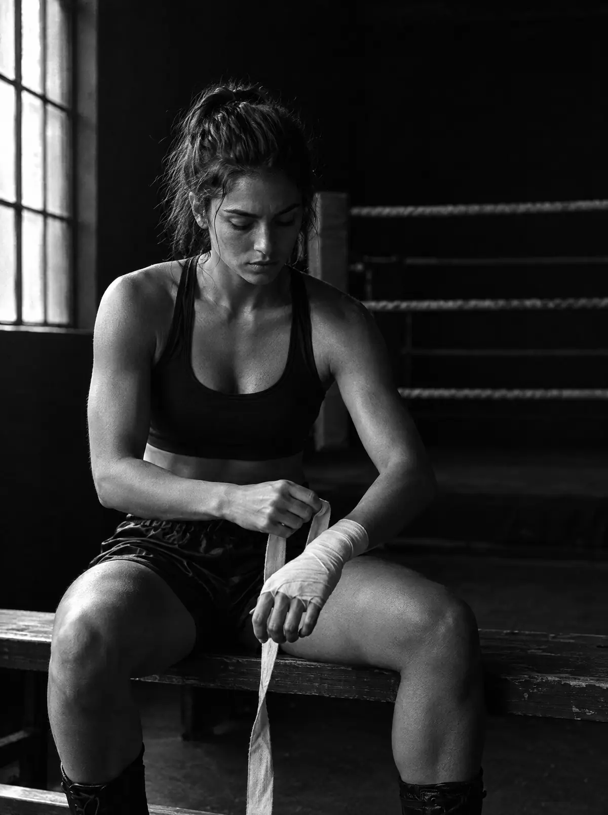 Boxeadora vendándose la mano en un gimnasio oscuro